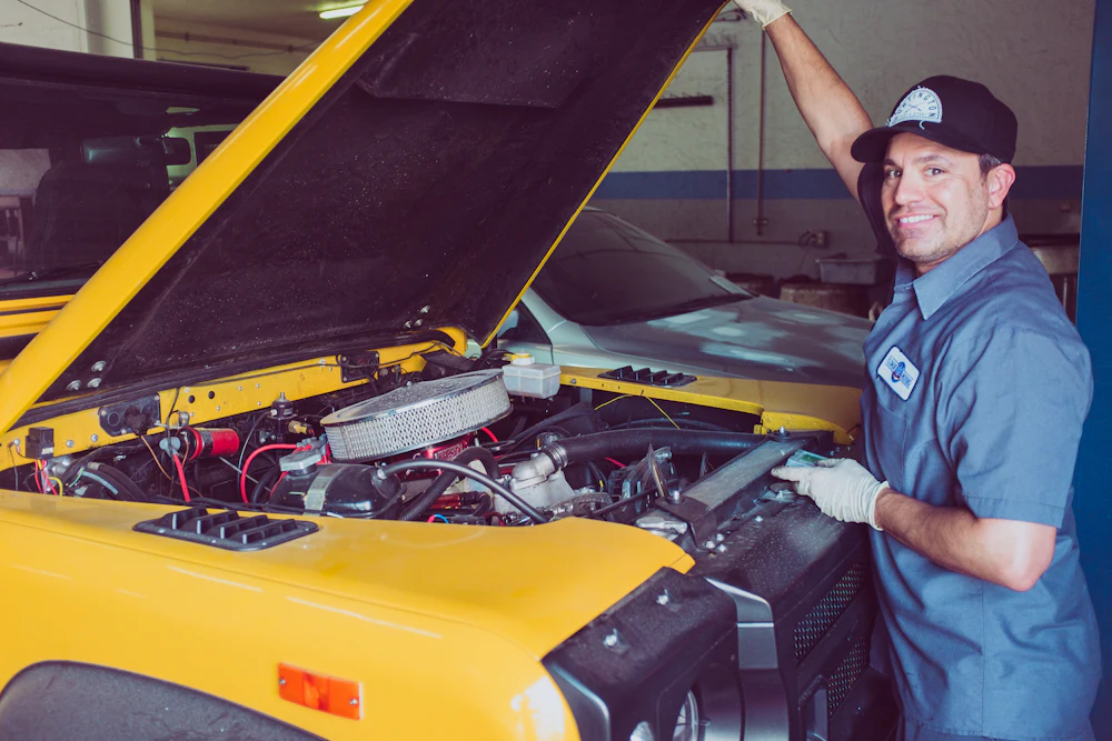 Smiling mechanic next to a car with the hood open